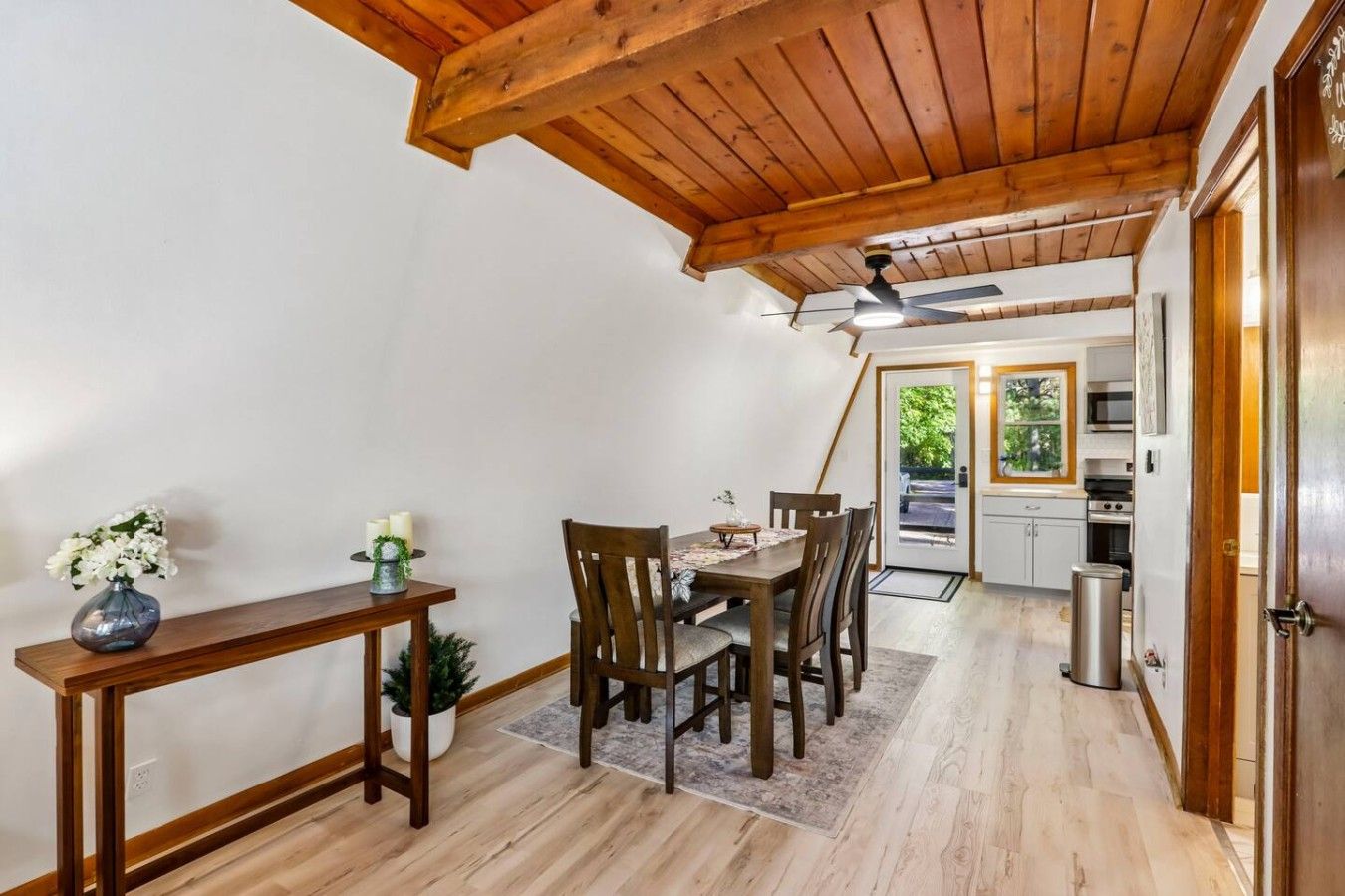 Un coin repas avec un plafond en bois, une table entourée de chaises, une petite plante en pot et un vase rempli de fleurs.