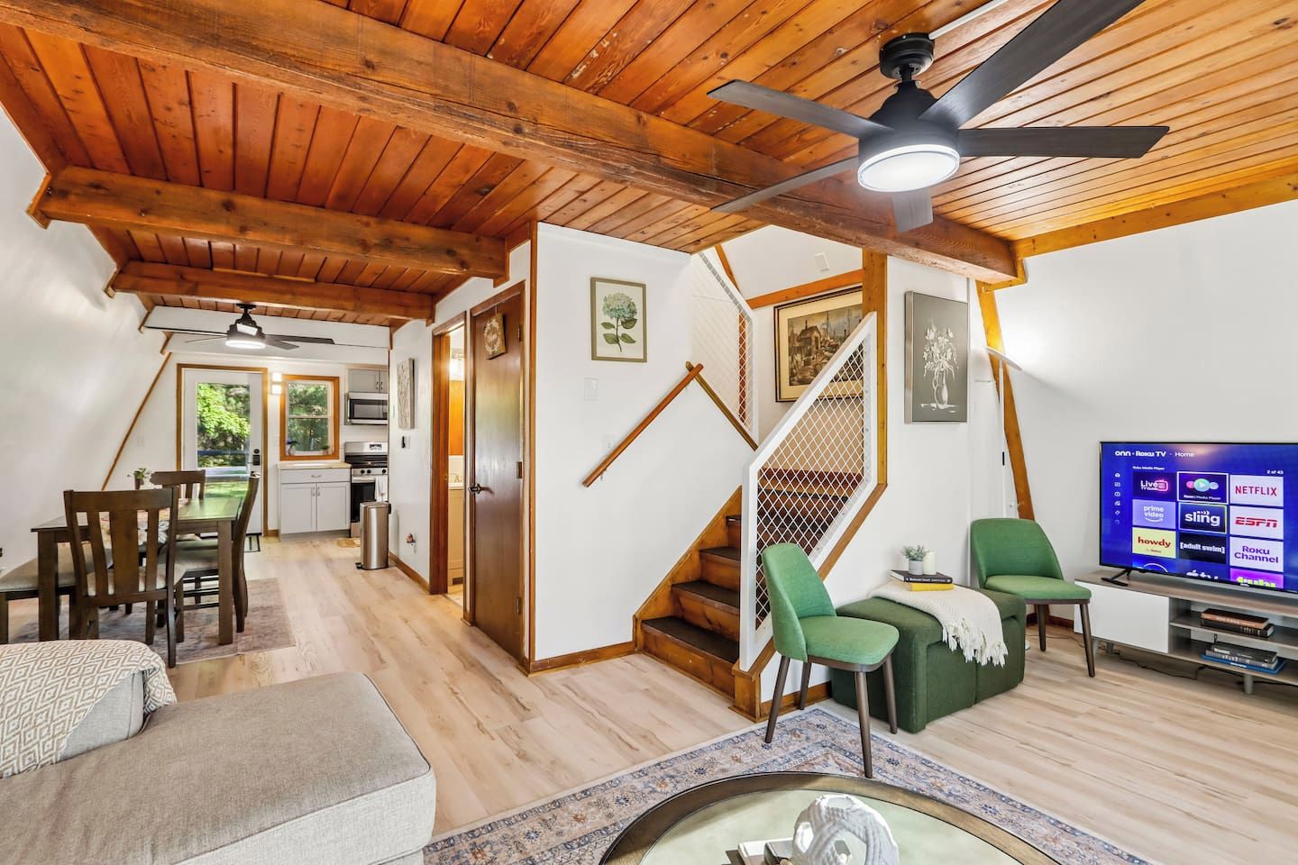 Un salon moderne avec un plafond en bois, un escalier, un coin repas et un téléviseur diffusant une chaîne de télévision.