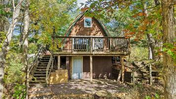 A cabin with a balcony, wooden stairs, and a door.