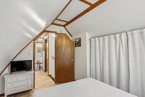 A bedroom with a sloped ceiling, a bed, a dresser, a television, and a door leading to another room. - Gem of an A-Frame; 10 minutes from Downtown Dells (Wisconsin Dells)