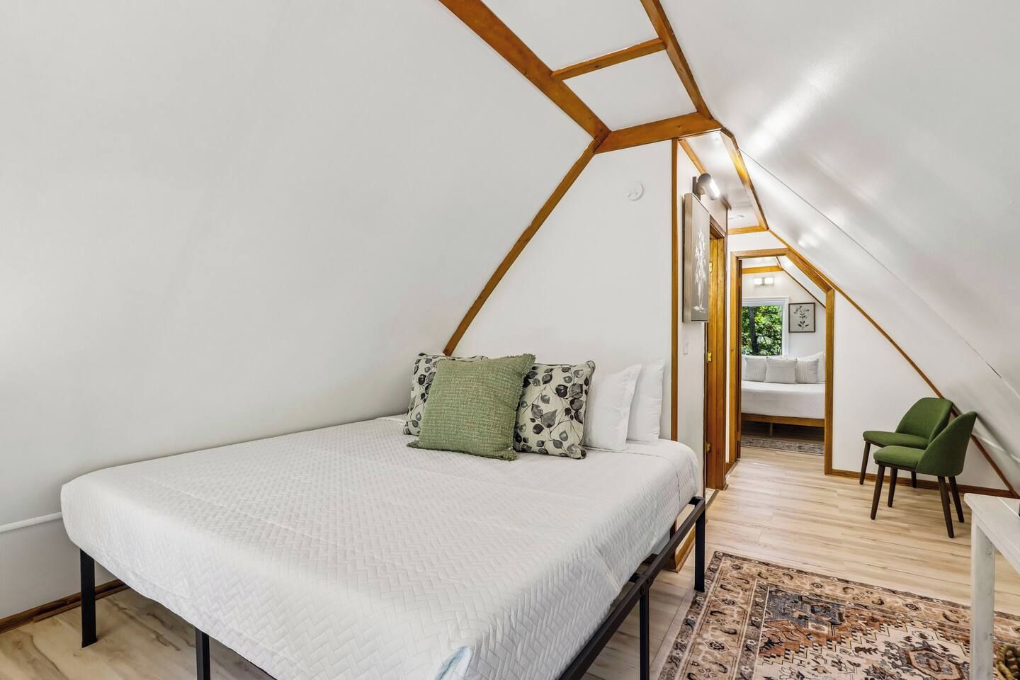 A bedroom with a bed, pillows, a chair, and a view into an adjacent room.