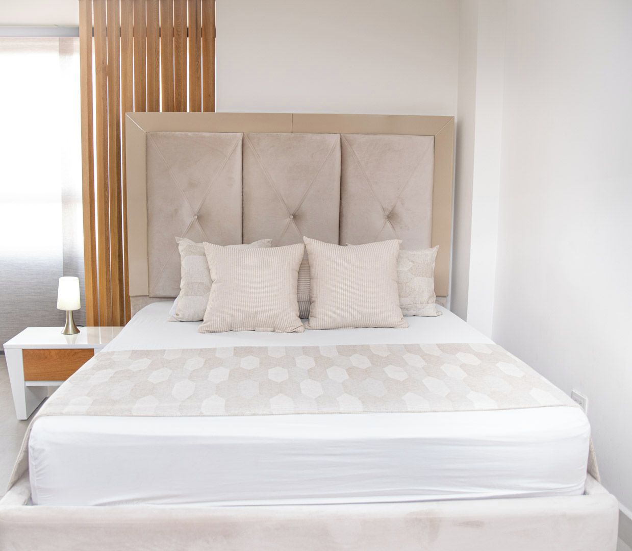 A hotel room with a large bed, a bedside table with a lamp, and a wooden slat wall.