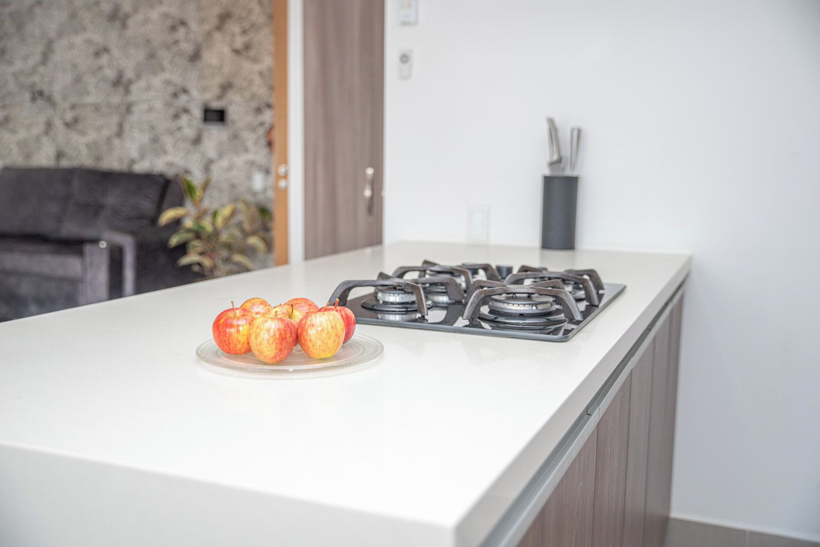 Una cucina moderna con un piano di lavoro bianco, un fornello a gas e un piatto di mele.