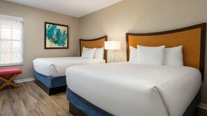 Una habitación de hotel con dos camas, un banco, un cuadro y una lámpara.