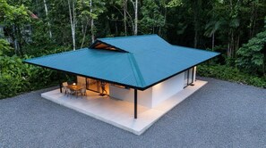 Ein modernes Haus mit Schrägdach, einer Terrasse mit Sitzgelegenheiten, umgeben von dichtem Wald.
