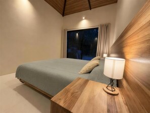 A bedroom with a bed, bedside table, lamp, and a window with curtains. - New Listing (Cocles)