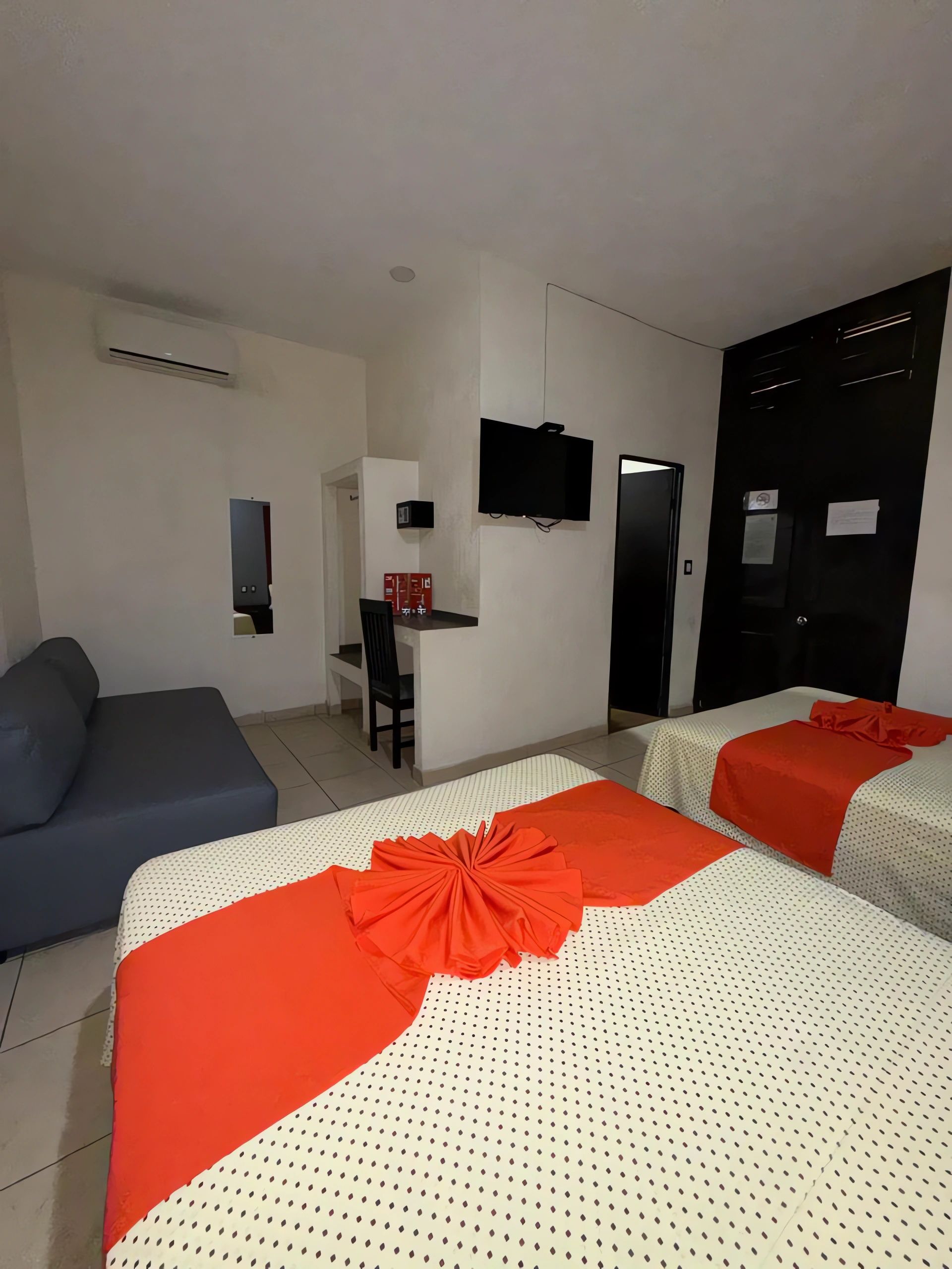 A hotel room with two beds, a sofa, a desk with a chair, and a television mounted on the wall.