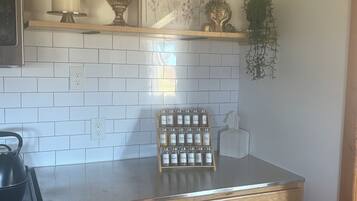 Una cocina con baldosas blancas tipo metro, estufa de acero inoxidable, armarios de madera, una obra de arte floral enmarco y una pequeña planta en maceta.