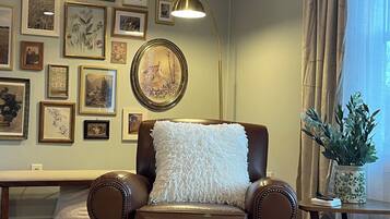 Un salón con un sillón de cuero marrón, un almohadón blanco mullido, un reposapiés redondo y una pared decorada con cuadros.