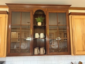 Un mueble de madera con puertas de vidrio, que contiene utensilios de cocina y una planta en maceta.
