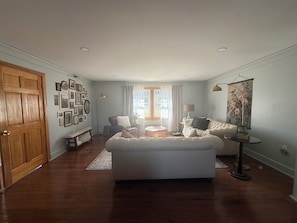 Een ruime woonkamer met een grote witte bank, een ronde salontafel en een houten vloer.