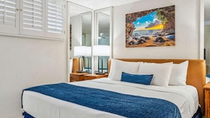 Una habitación de hotel con una cama, una mesita de noche, una lámpara y un cuadro de una playa.