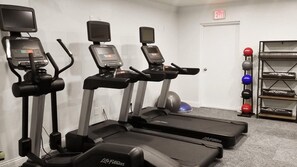 Three treadmills, a weight rack with various weights, and an exit sign in a fitness room.