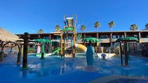 A water park with slides and a pool area, surrounded by palm trees and a hotel building.