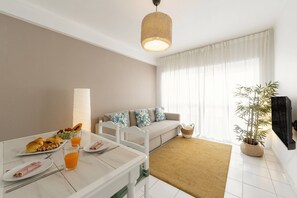A modern living room with a sofa, a dining table with breakfast, and a large window with curtains. - Balance House Surf in Peniche (Peniche)