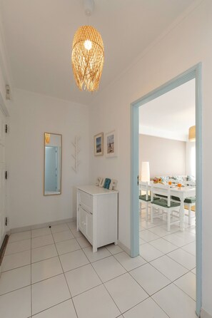 A bright, modern room with white walls, a white cabinet, a mirror, and a hanging light fixture. - Balance House Surf in Peniche (Peniche)