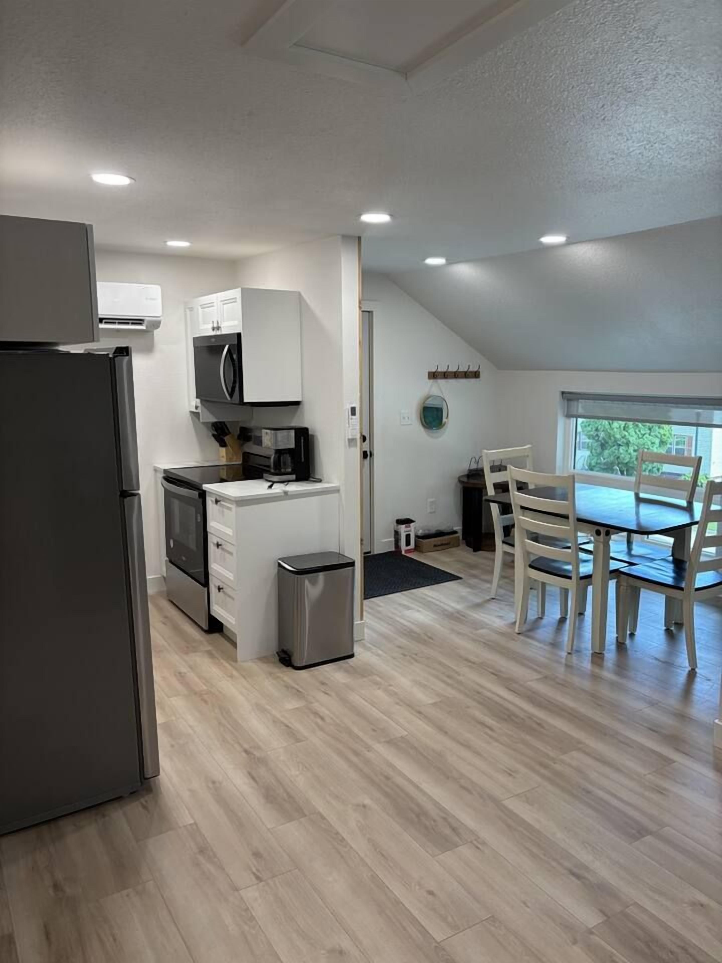 A compact kitchen with a refrigerator, microwave, and stove, a small trash bin, and a dining area with a table and chairs.