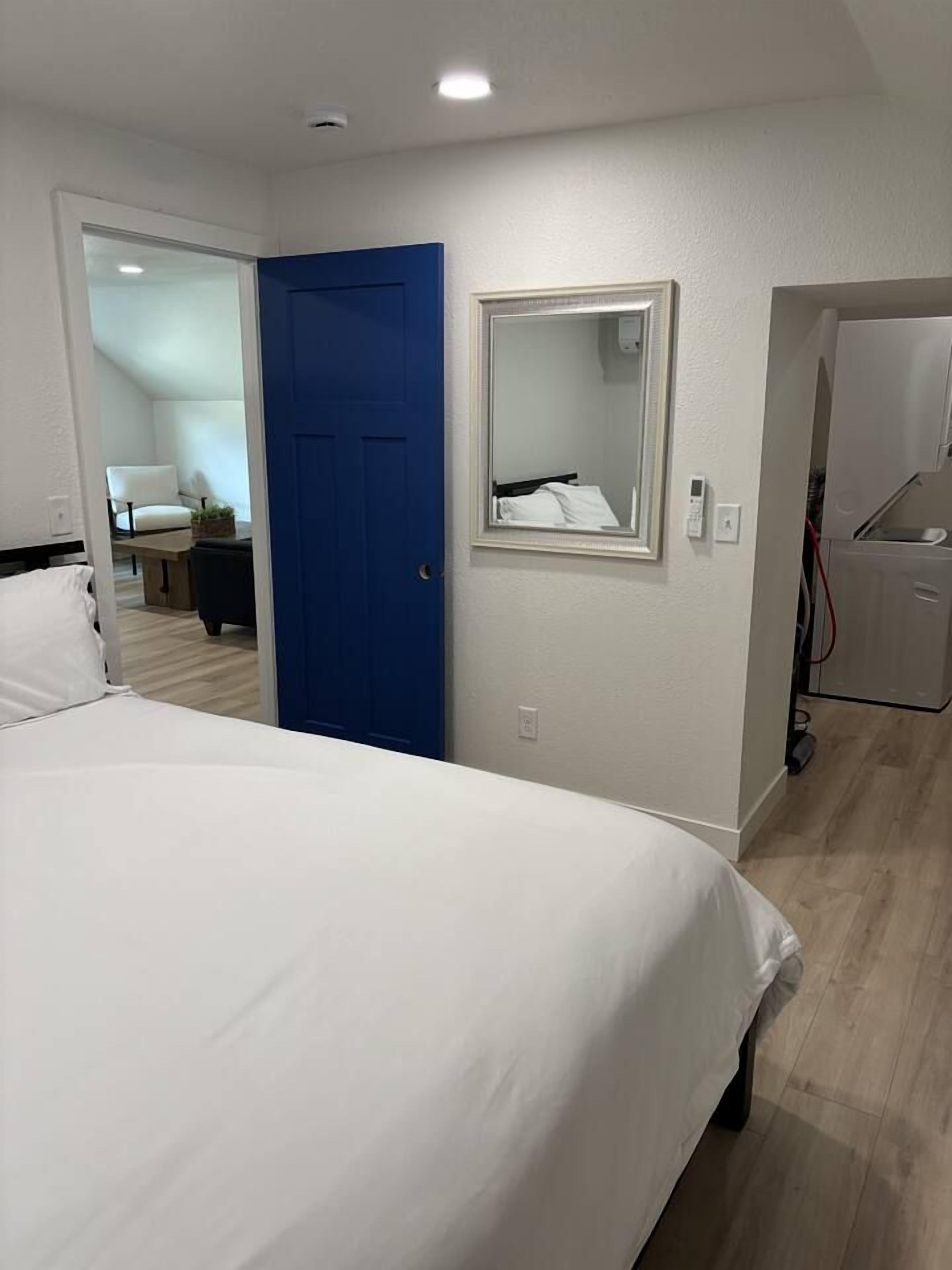 A hotel room with a bed, a blue door, a mirror, and a kitchenette.