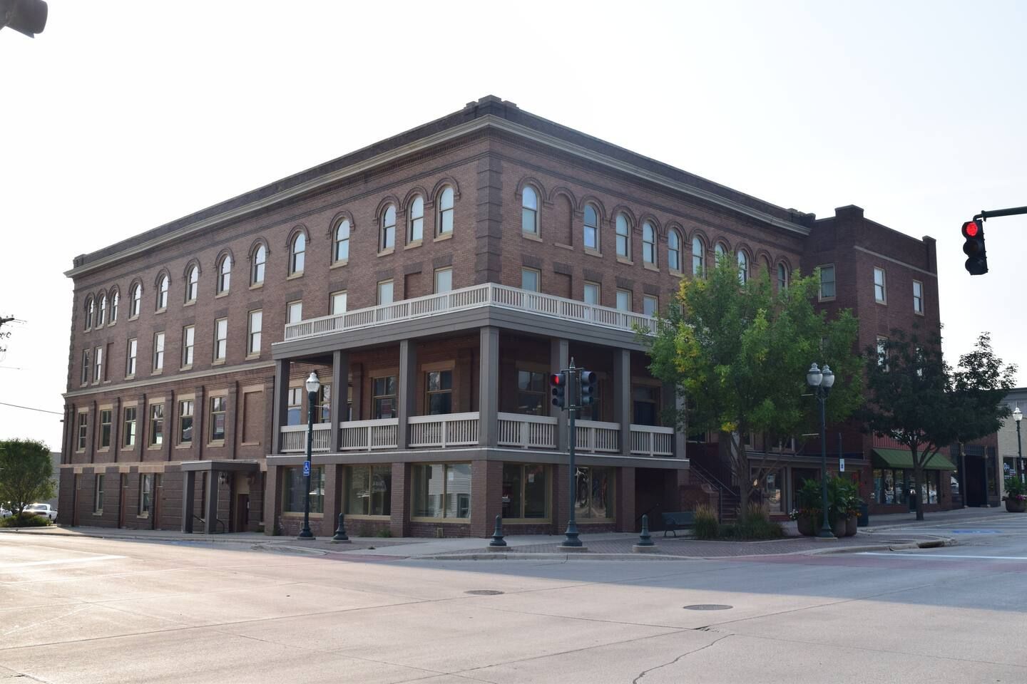 A multi-story brick building with a balcony on the ground floor, a clear sky, and a traffic light.