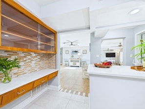 Une cuisine moderne avec des meubles en bois, un îlot central doté d’une façade en verre et un coin repas équipé d’un téléviseur.