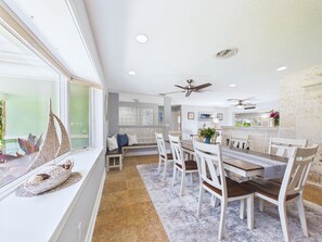 A dining area with a long table, white chairs, and a view through a large window. - Boater s Paradise Dock Hot Tub Cocoa Beach (Cocoa Beach)