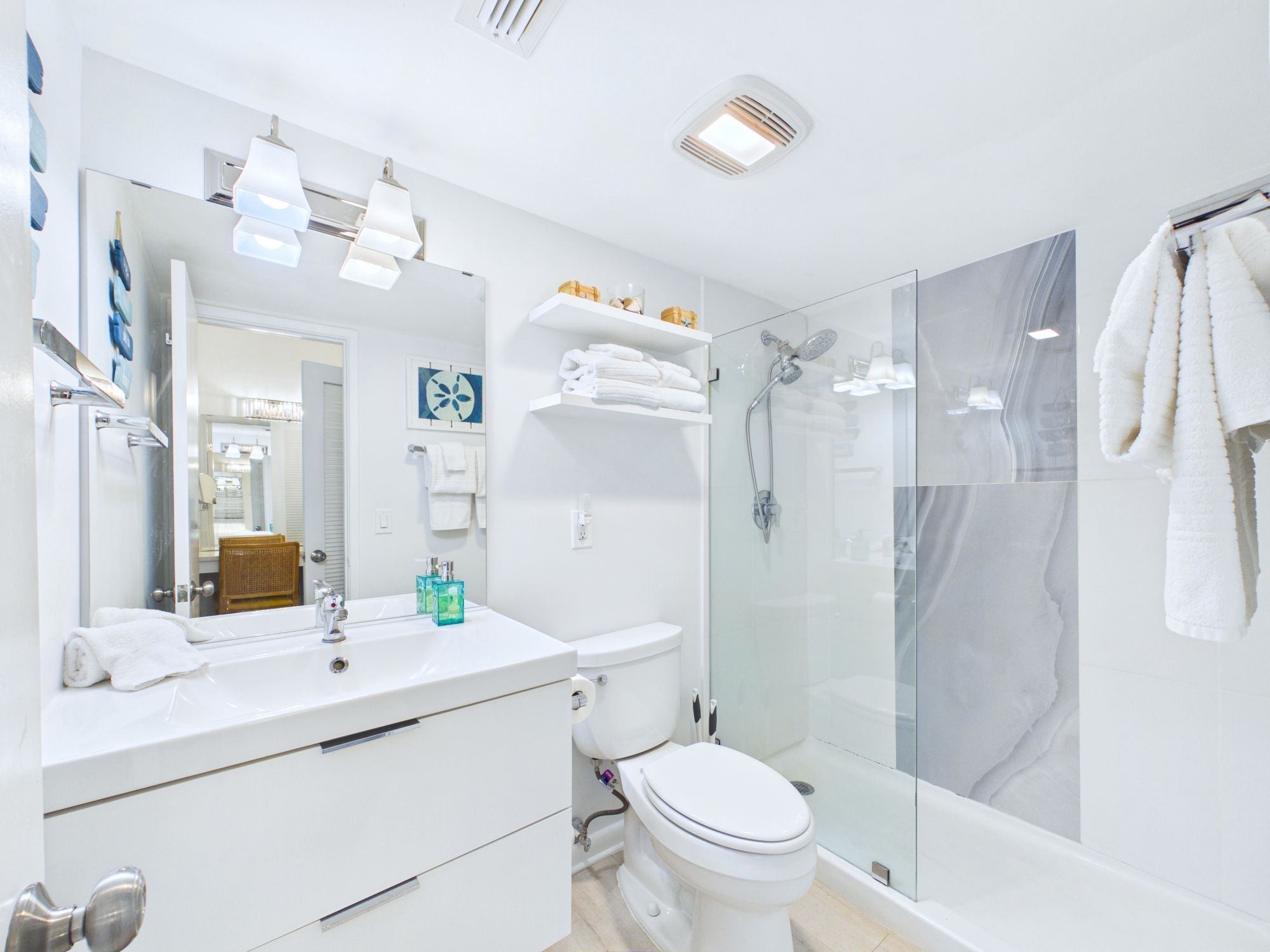 A modern bathroom with a glass-enclosed shower, white fixtures, and a large mirror.
