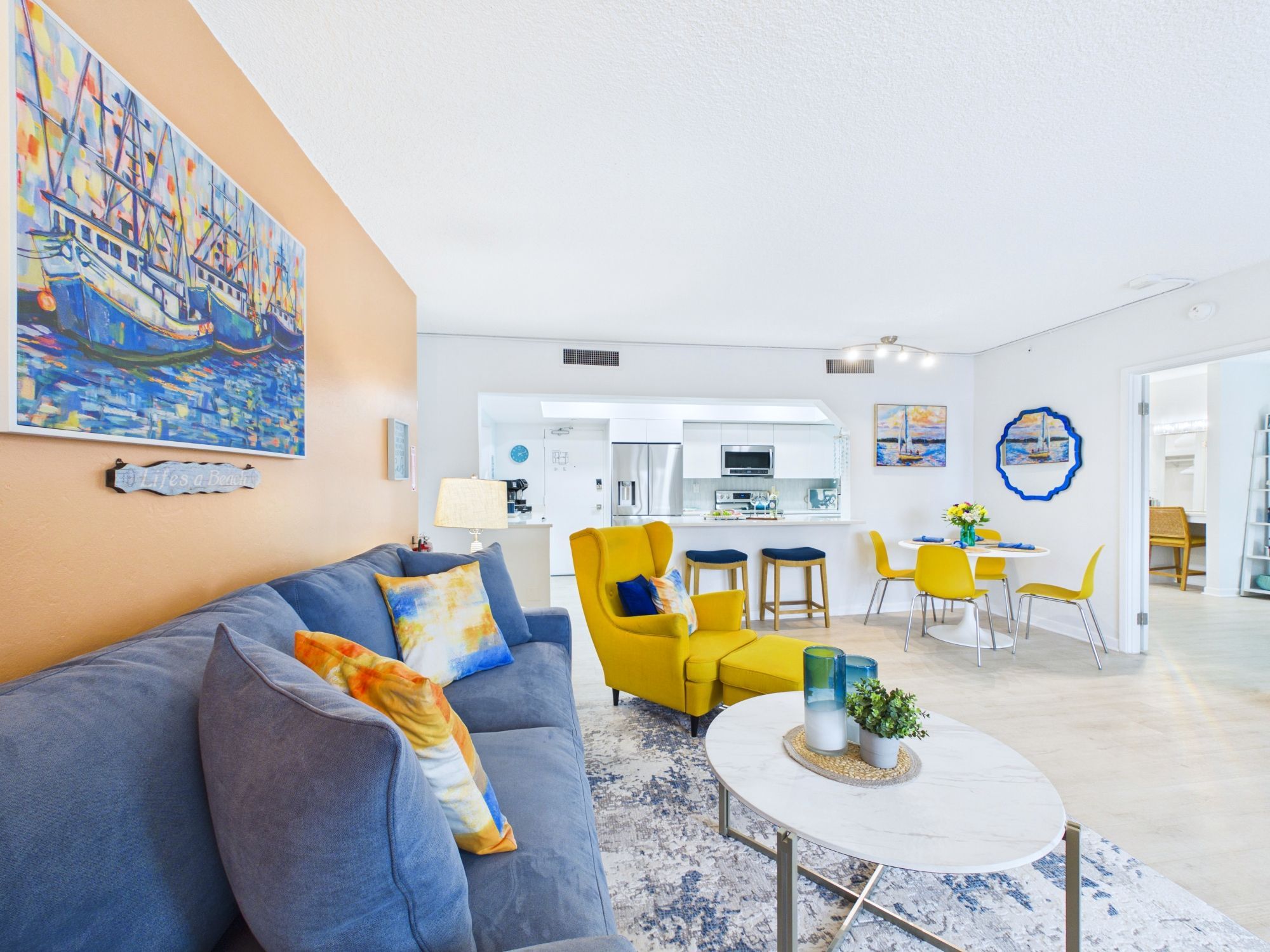 A modern living room with a sofa, armchairs, a dining area, and a kitchen.