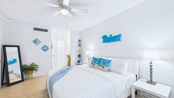 Un dormitorio con cama, mesita de noche, lámpara, ventilador de techo y decoración mural.