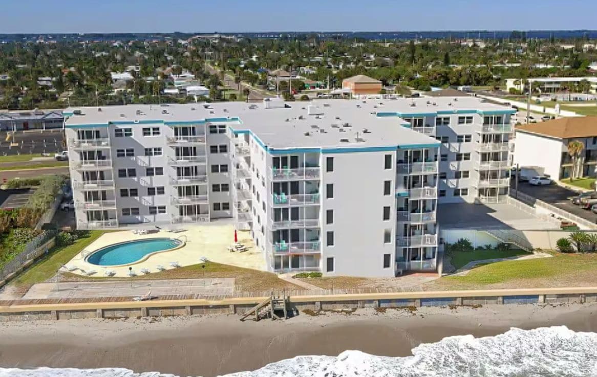 A multi-story residential building with a swimming pool and a beach view.
