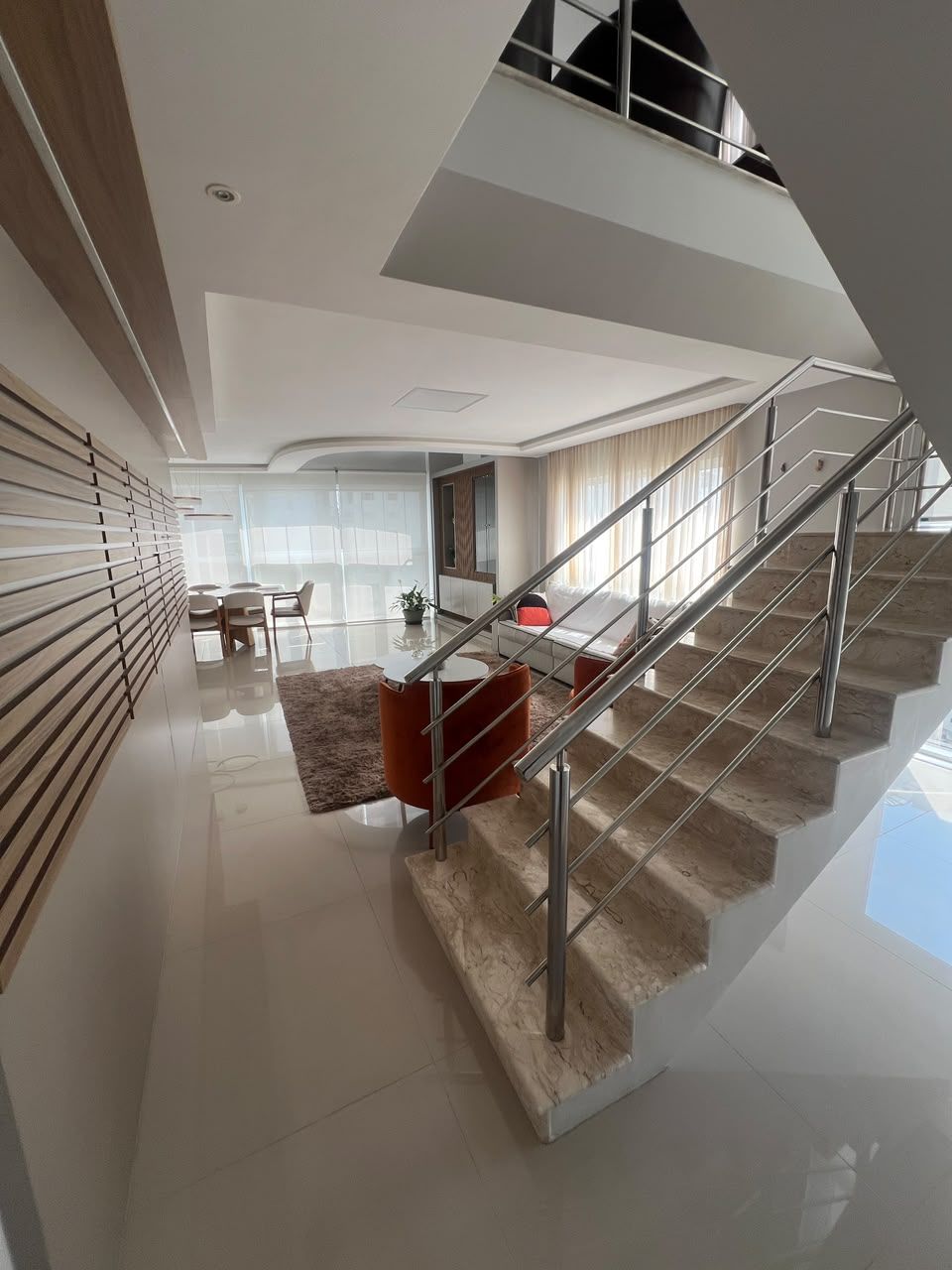 A modern interior with a staircase leading to an upper level, a dining area with a table and chairs, and a view of the outdoors.