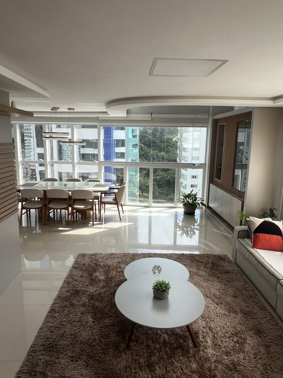 A modern living room with a dining area, large windows, and a view of buildings.