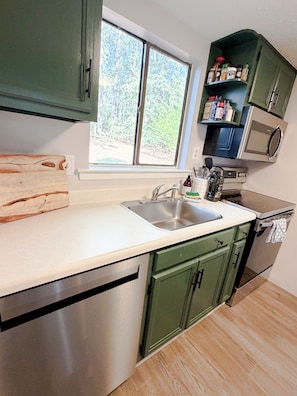 A kitchen with a built-in microwave, stainless steel appliances, a window with a view of greenery, and a spice rack. - Pinehurst Poolside Retreat - Steps to Lake Pinehurst - 2 BR Condo (Pinehurst)
