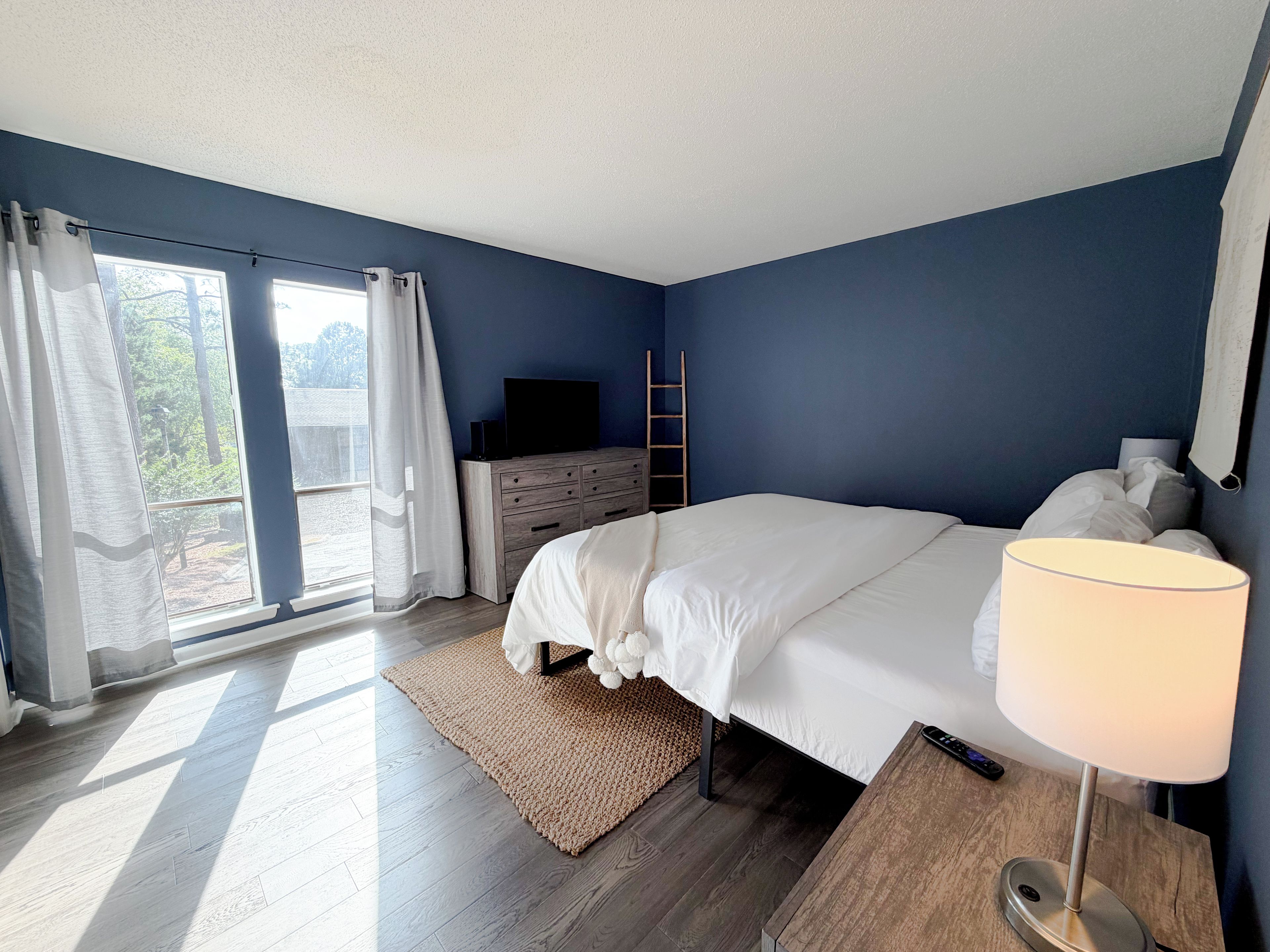 Une chambre à coucher avec un lit, une télévision, une commode, une lampe et une vue par la fenêtre.