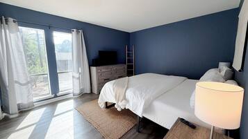 Une chambre à coucher avec un lit, une télévision, une commode, une lampe et une vue par la fenêtre.