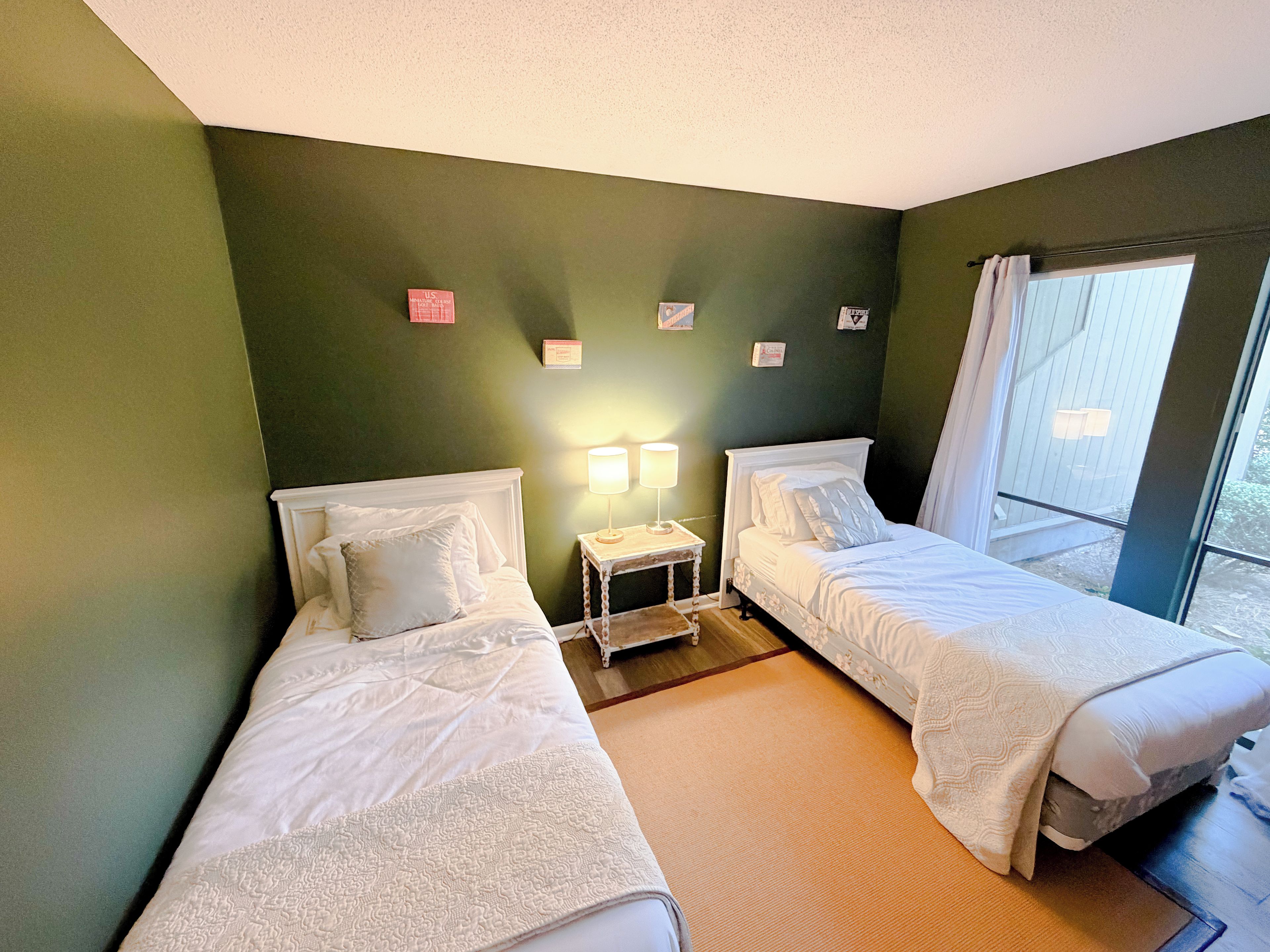 A room with two single beds, a nightstand with a lamp, and a window with curtains.