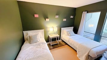 A room with two single beds, a nightstand with a lamp, and a window with curtains.