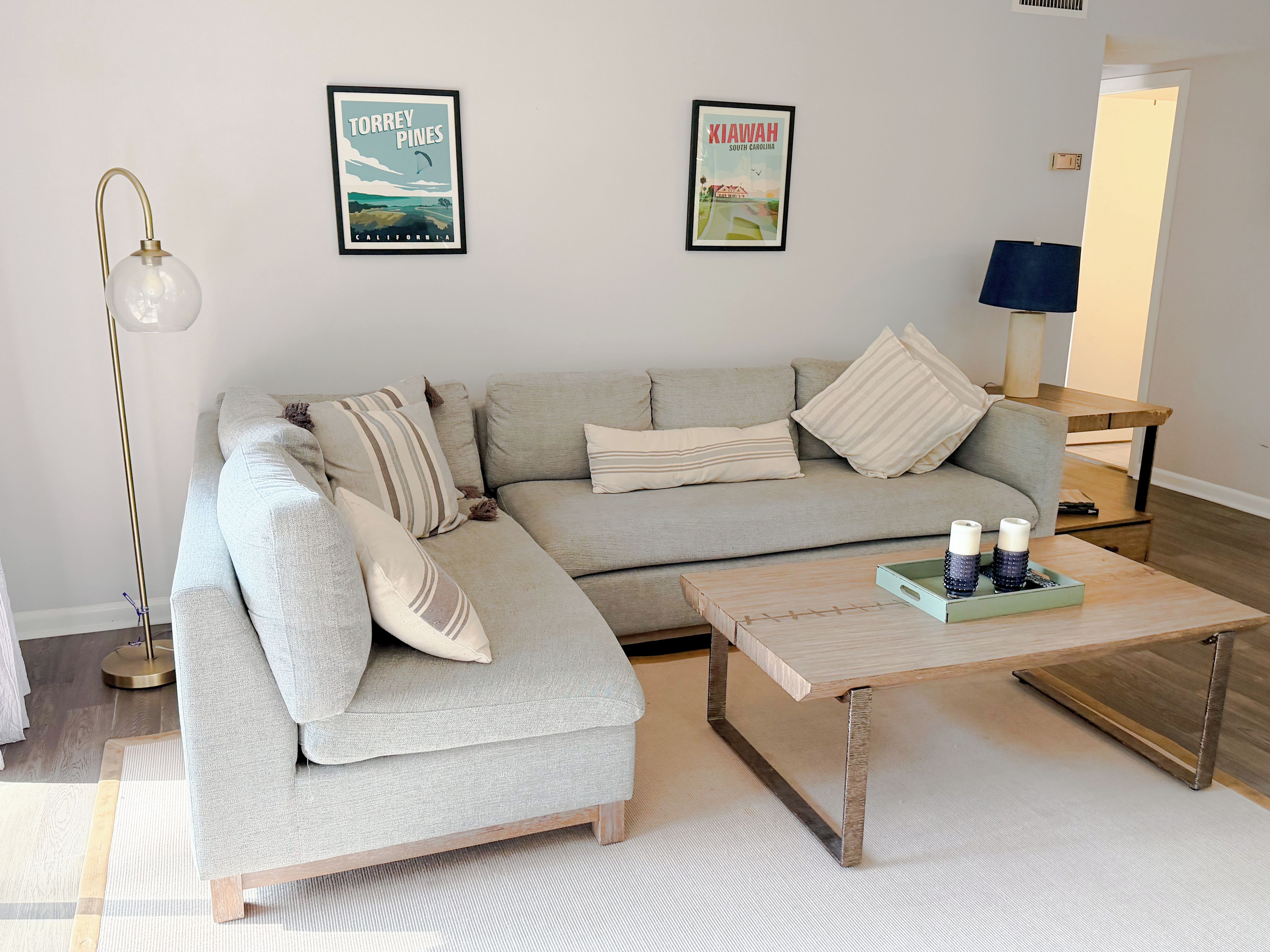 Un salon moderne avec un canapé d’angle, une table basse et deux affiches encadrées au mur.