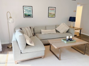 A modern living room with a sectional sofa, a coffee table, and two framed posters on the wall. - Pinehurst Poolside Retreat - Steps to Lake Pinehurst - 2 BR Condo (Pinehurst)