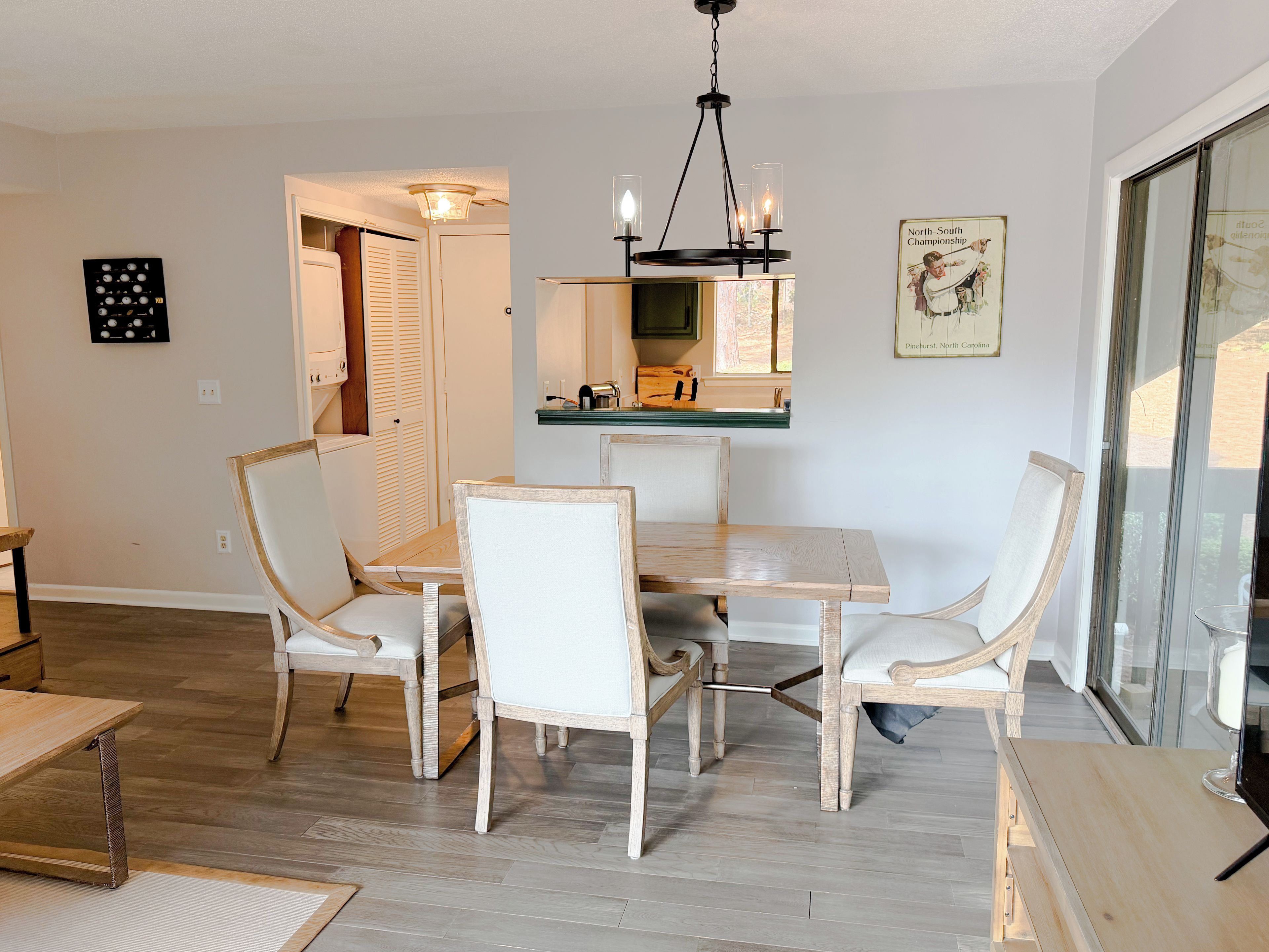 A dining area with a wooden table and chairs, a chandelier, and a framed picture on the wall.