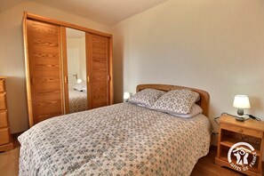 A bedroom with a bed, wooden wardrobe, bedside table, and a lamp. - The Song of the Waves 2 (PLOUHA)