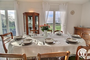 Uma sala de jantar com mesa posta para seis pessoas, um armário de madeira e vista para o exterior.