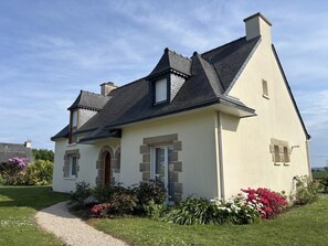 A two-story house with a steeply pitched roof, a stone foundation, and a front entrance with a door and windows. - The Song of the Waves 2 (PLOUHA)