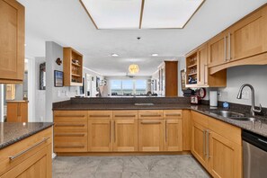 A modern kitchen with wooden cabinets, granite countertops, and a built-in dishwasher. - Oceanfront Condo | Balcony, Pool & Beach (Daytona Beach Shores)