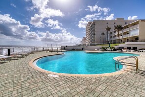 A swimming pool with a curved edge, surrounded by lounge chairs and a brick deck. - Oceanfront Condo | Balcony, Pool & Beach (Daytona Beach Shores)