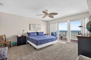 Ein Schlafzimmer mit Bett, Nachttisch, Stuhl, Schreibtisch, Globus und einem Balkon mit Meerblick.