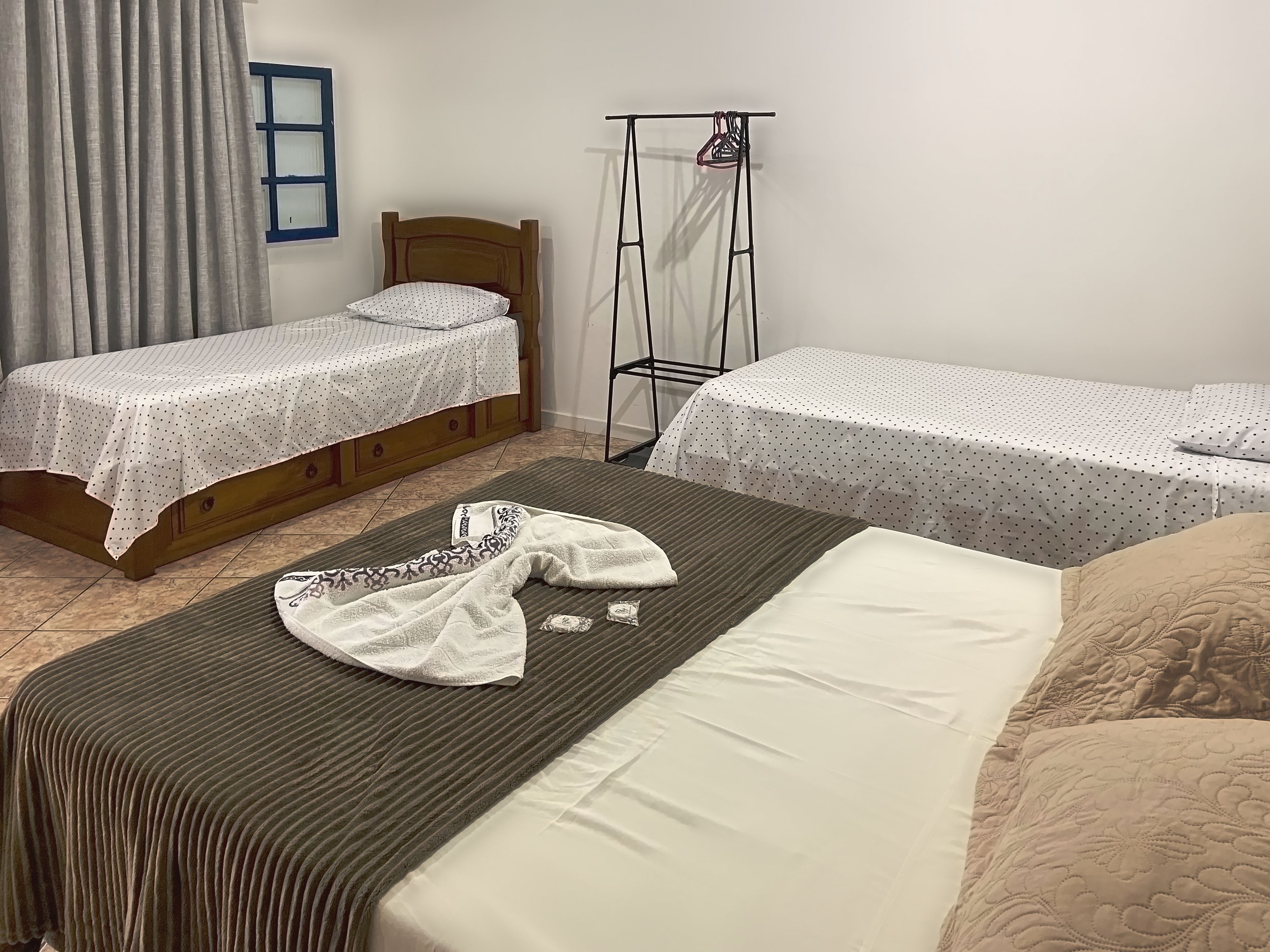 A room with two single beds, a wooden headboard, a bed with a striped cover, and a clothing rack.