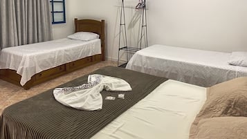 A room with two single beds, a wooden headboard, a bed with a striped cover, and a clothing rack.