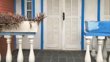 Fachada de edificio con puerta blanca, detalles azules y una maceta con plantas.