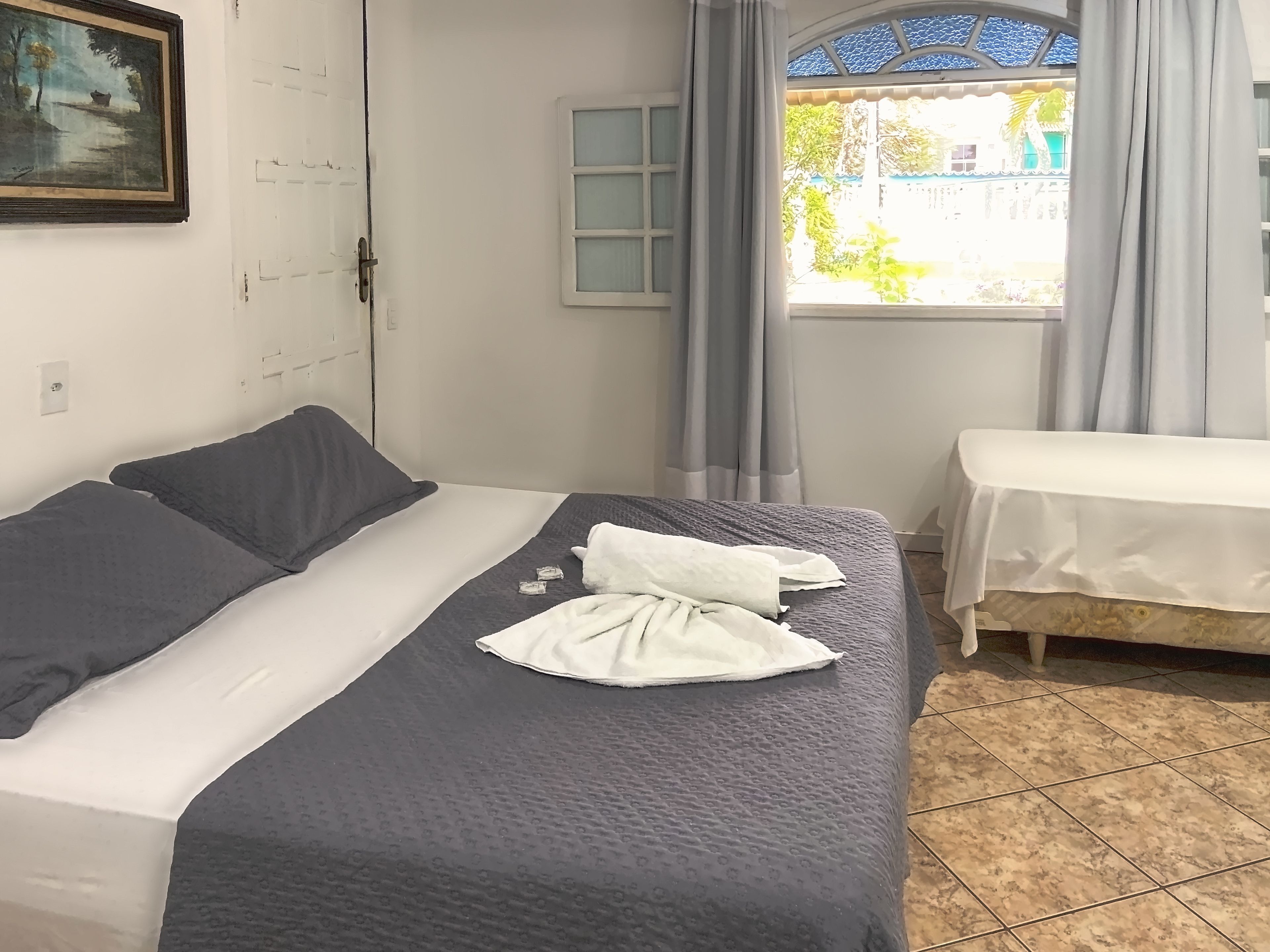 Una habitación de hotel con una cama, una mesita, una ventana con cortinas y un cuadro en la pared.