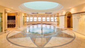 A spacious indoor pool with a central fountain, surrounded by a circular tiled floor with a decorative pattern. - Villa del Arco Beach Resort - Oceanfront 3BR on Medano Beach, Cabo (Cabo San Lucas)
